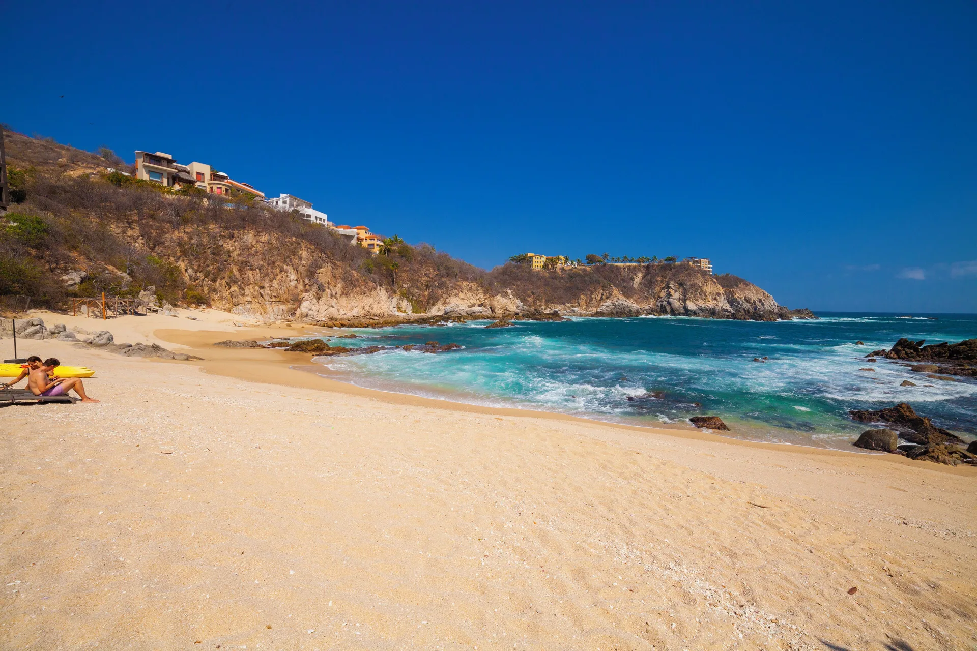 Sandy beach with turquoise surf and rocky cliffs at Coral Blue Huatulco.