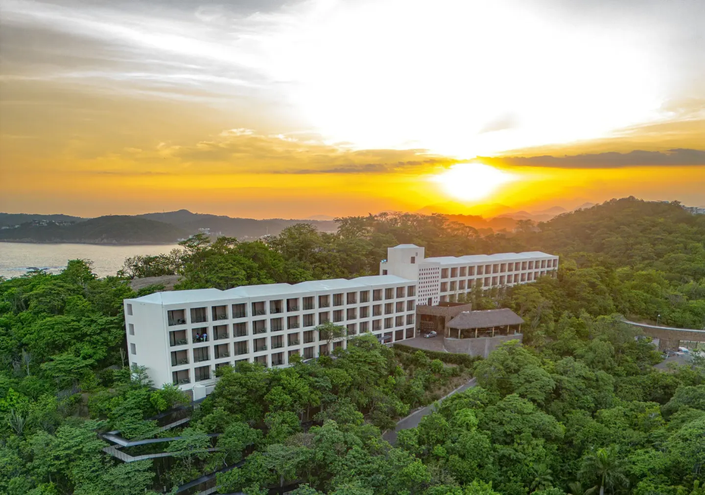 Sunset over Coral Blue Huatulco with a white hillside building and surrounding trees.
