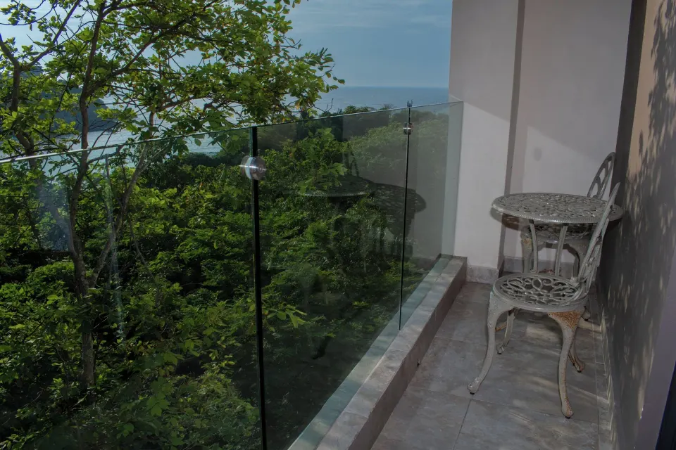 Private balcony with glass railing, table and chair in a Deluxe Room at Coral Blue Huatulco.