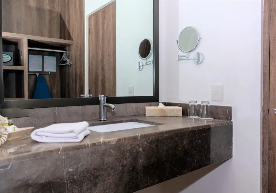 Bathroom vanity with sink, mirror, towels and glasses in a Deluxe Room at Coral Blue Huatulco.