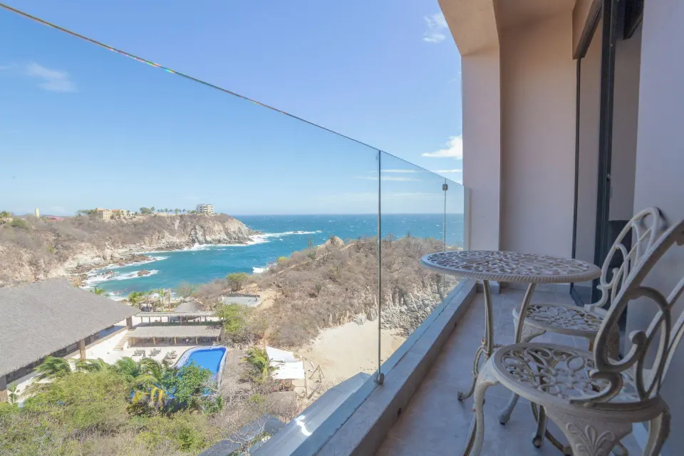 Balcony with table, chairs, and partial ocean view at Coral Blue Huatulco.