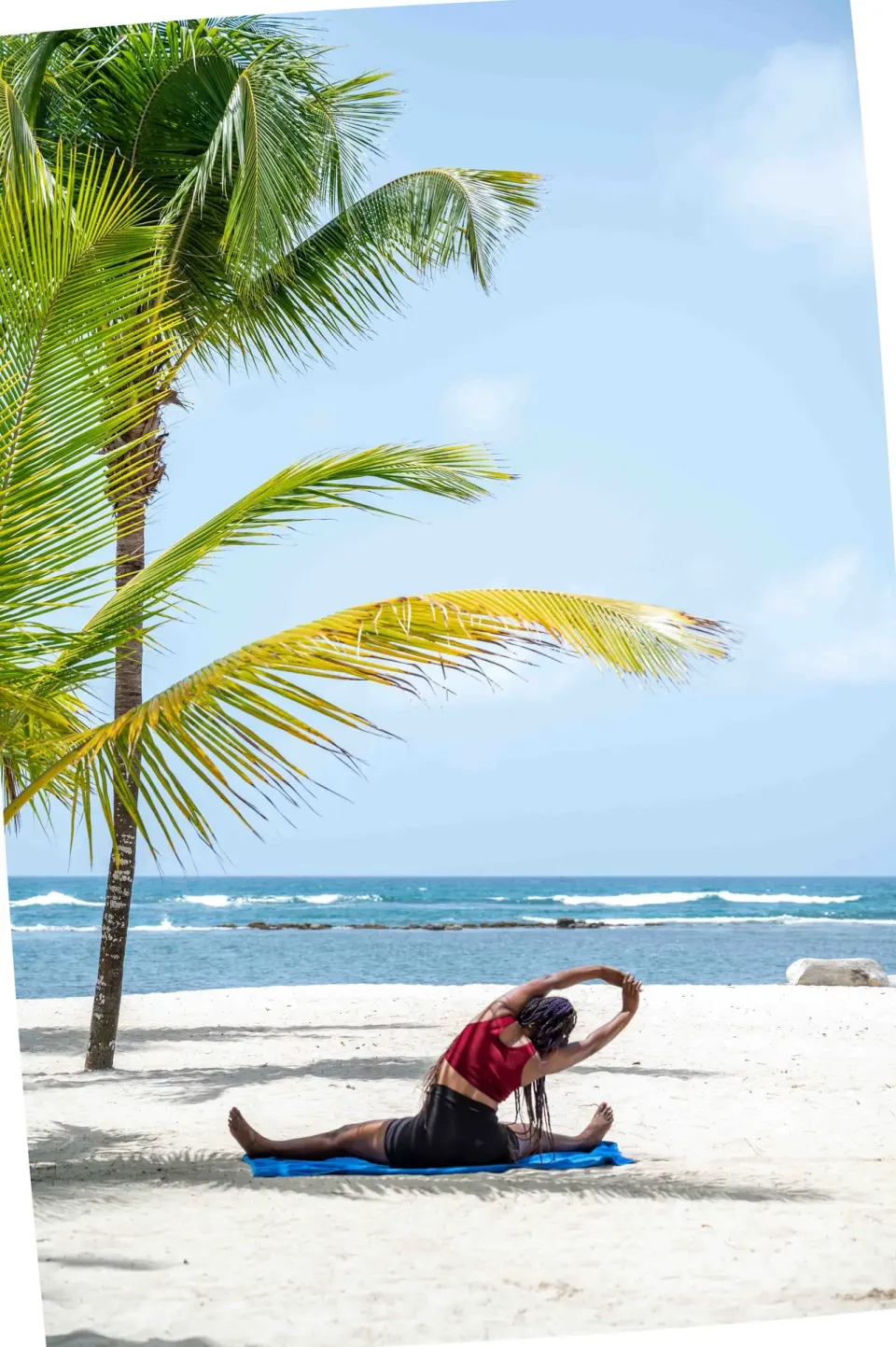 Person stretching on a beach mat under a palm tree at Coral Costa Caribe Beach Resort.