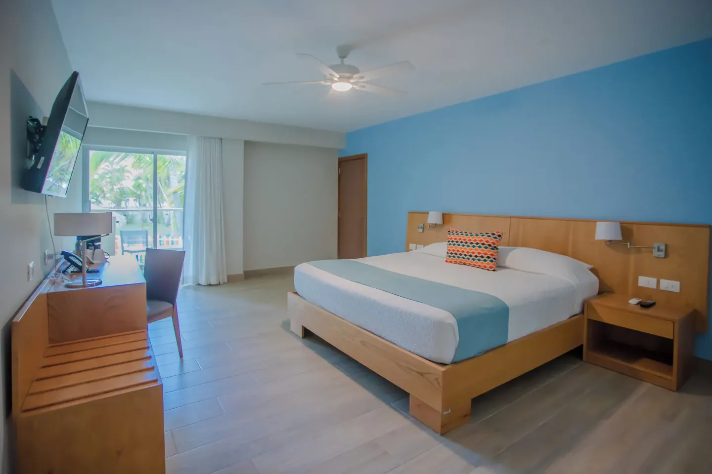 Deluxe Room king bed with blue accent wall and balcony at Coral Costa Caribe Beach Resort.