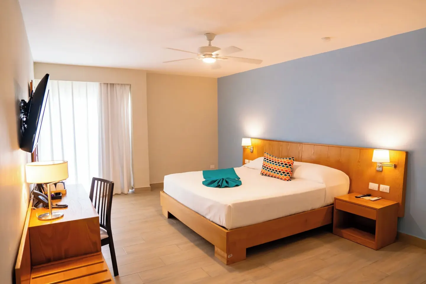 Deluxe Room king bed with blue wall, desk, and ceiling fan at Coral Costa Caribe Beach Resort.