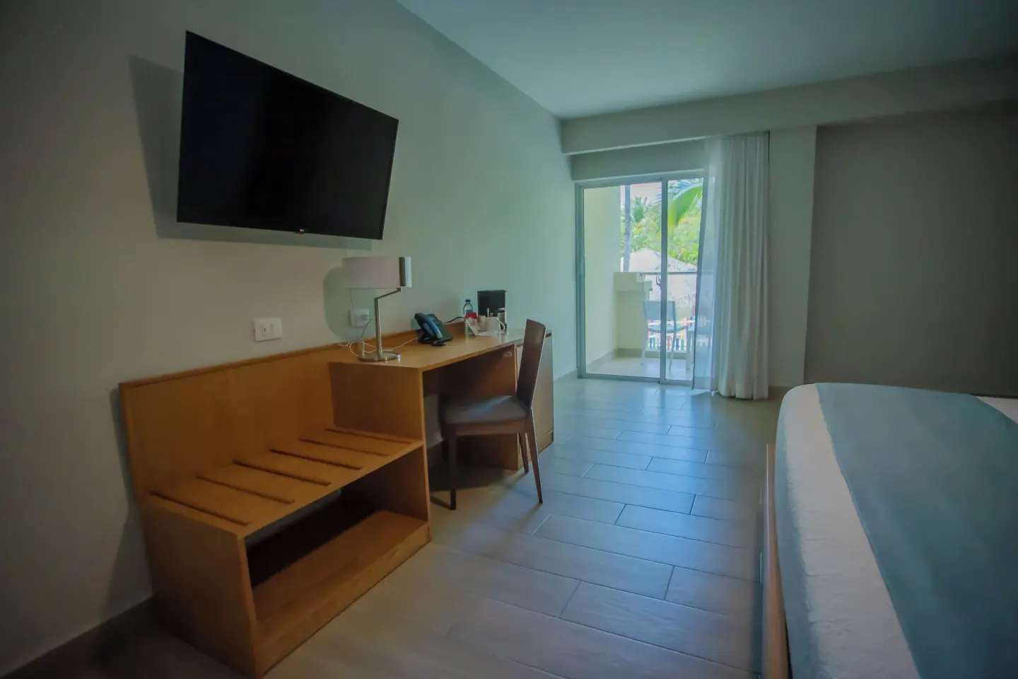 Deluxe Room with balcony, desk, TV, and bed edge at Coral Costa Caribe Beach Resort.