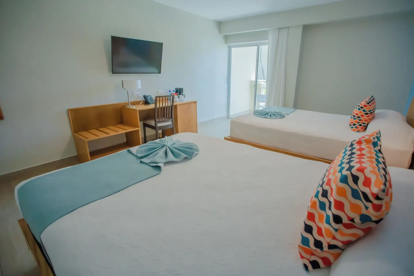 Deluxe Room two beds with towel accents and balcony doors at Coral Costa Caribe Beach Resort.