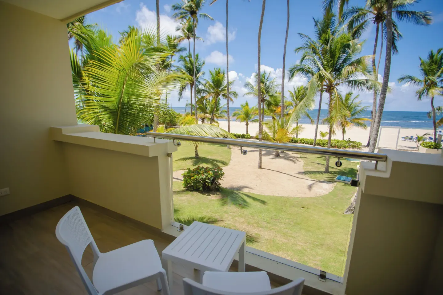 Room balcony with white chairs, table, palms, beach, and ocean at Coral Costa Caribe Beach Resort.