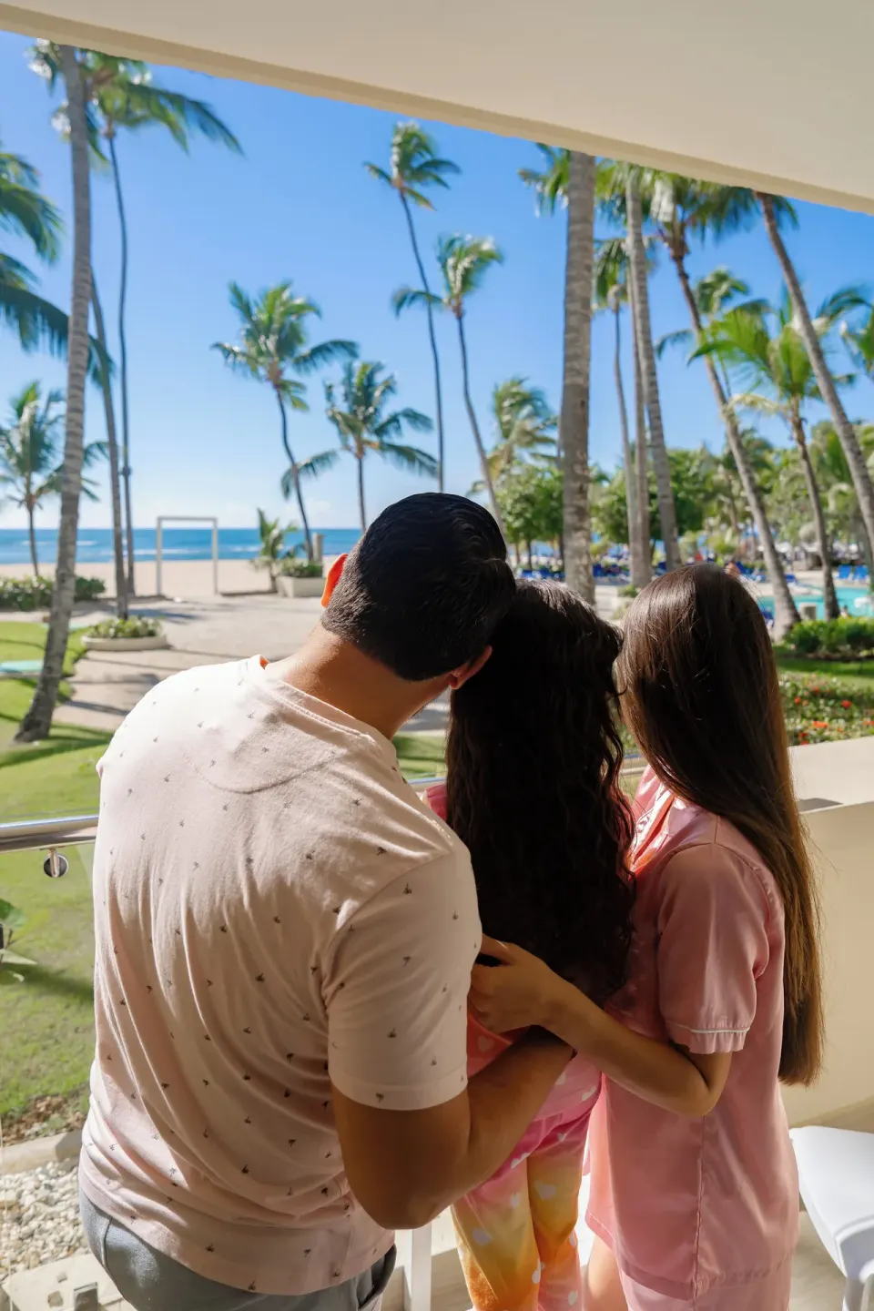 Family on a room balcony overlooking palms and the beach at Coral Costa Caribe Beach Resort.