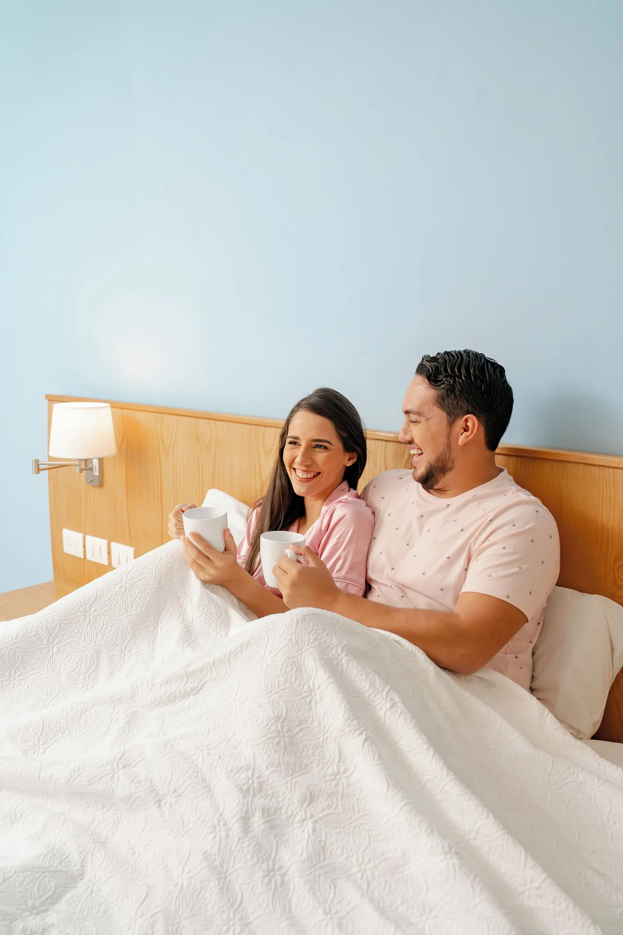 Couple holding cups in bed in a Standard Room at Coral Costa Caribe Beach Resort.