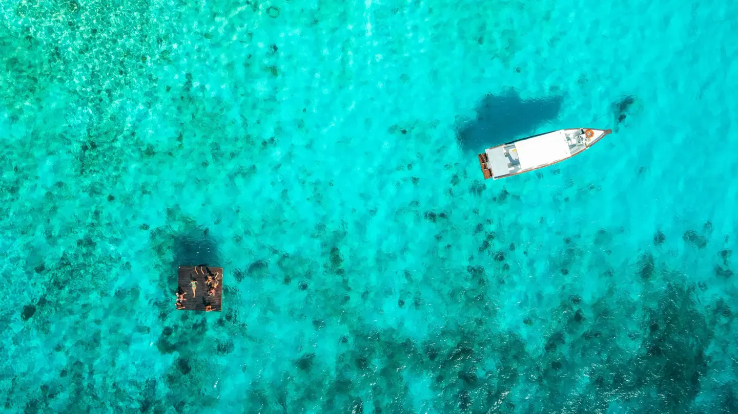 Aerial view of a small boat and swim platform in turquoise water at Coral Estate Luxury Resort.