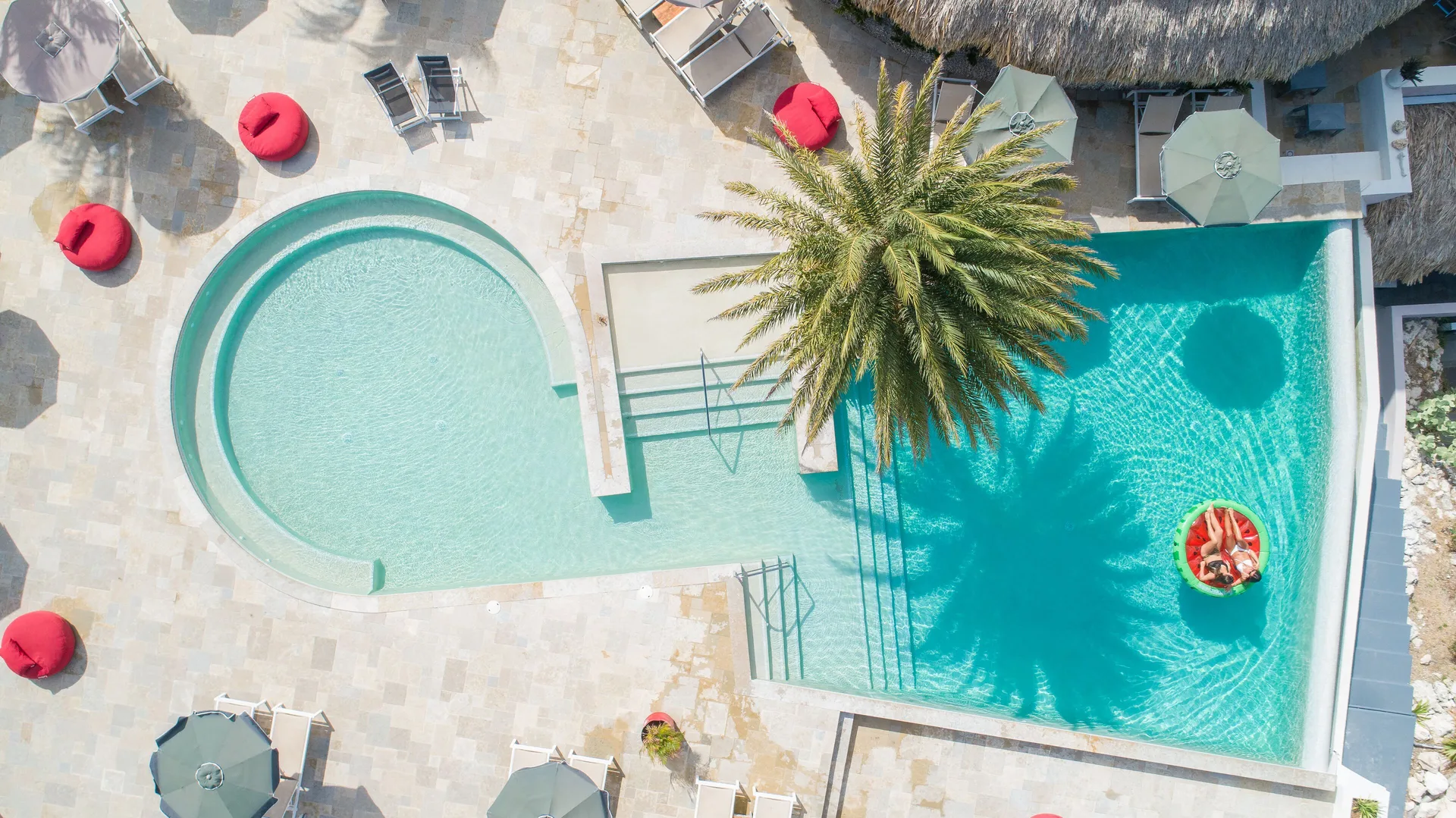 Overhead view of the pool with loungers, umbrellas, red seats and a palm at Coral Estate Luxury Resort.