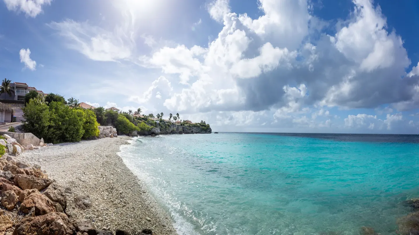 Curving pebble beach and turquoise sea at Coral Estate Luxury Resort under a bright sky.