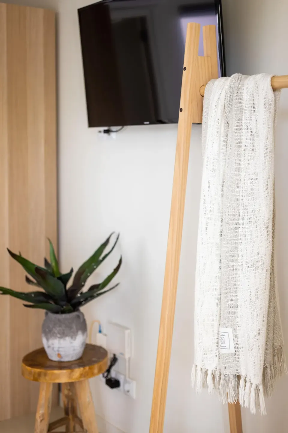 A towel ladder, wall-mounted TV, wood cabinet and potted plant in a room at Coral Estate Luxury Resort.