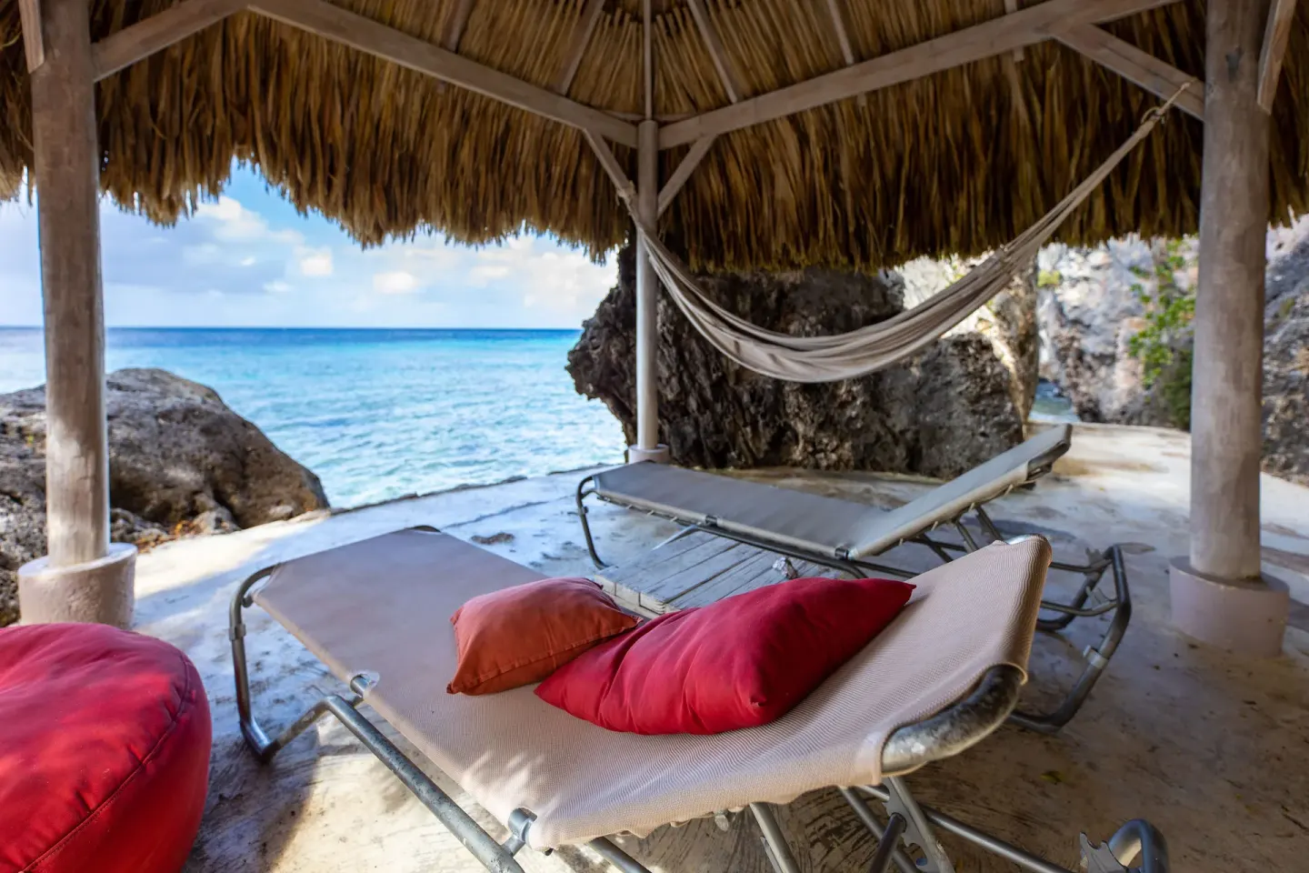 Shaded seaside loungers and a hammock under a thatched shelter at Coral Estate Luxury Resort.