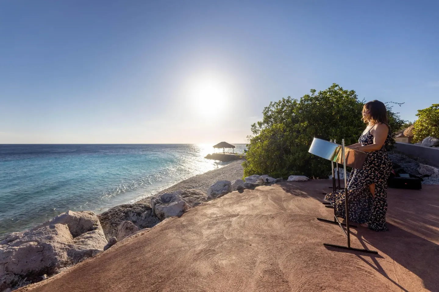 Woman painting beside the rocky shoreline at Coral Estate Luxury Resort at sunset.