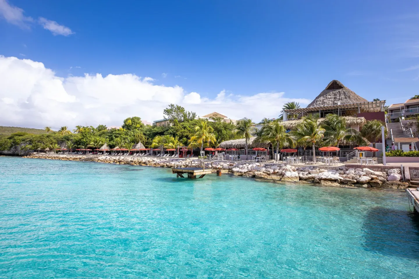 Turquoise waterfront and resort terraces at Coral Estate Luxury Resort with red umbrellas.