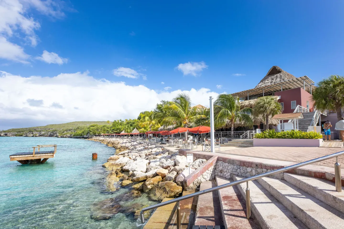 Waterfront terraces and rocky shoreline at Coral Estate Luxury Resort beside clear blue water.