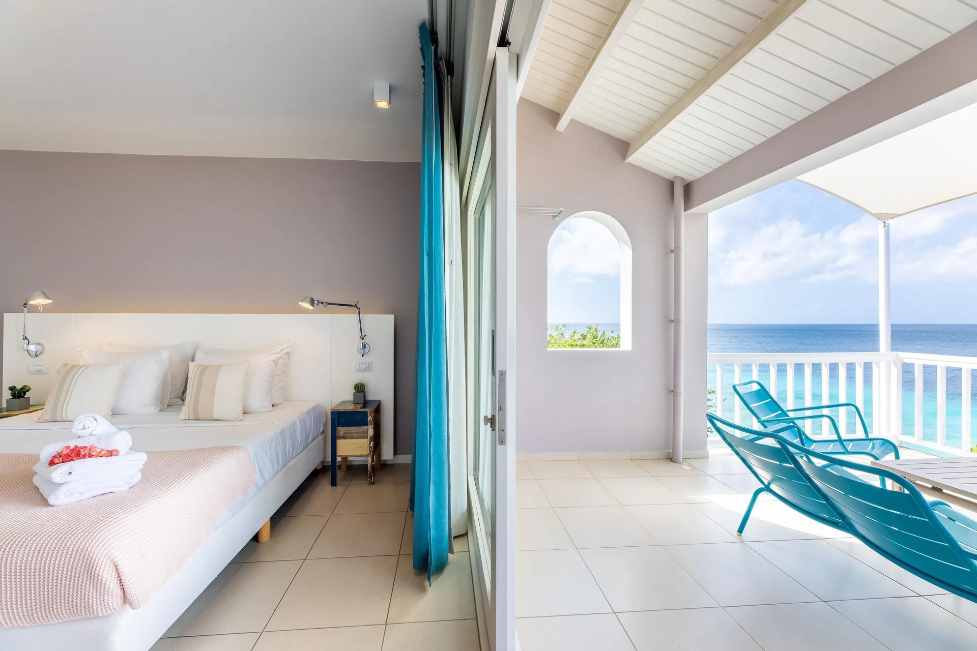 Deluxe Room Ocean View bed beside a covered balcony at Coral Estate Luxury Resort.