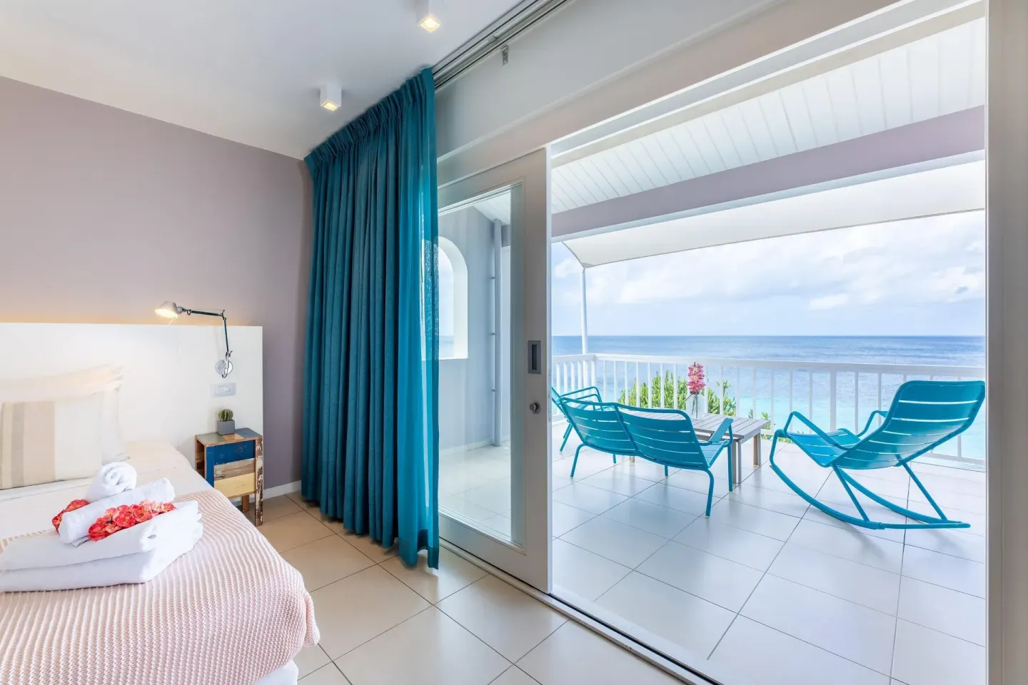 Deluxe Room Ocean View with bed, blue curtains, and sea-facing terrace at Coral Estate Luxury Resort.