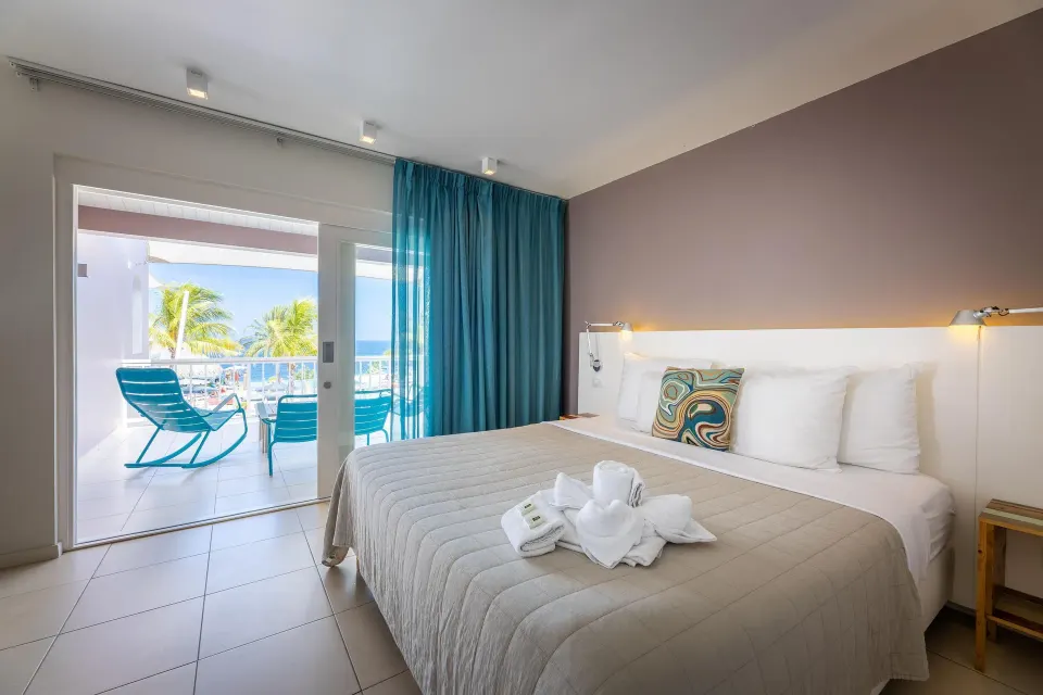 Deluxe Room king bed and balcony with ocean glimpse at Coral Estate Luxury Resort.