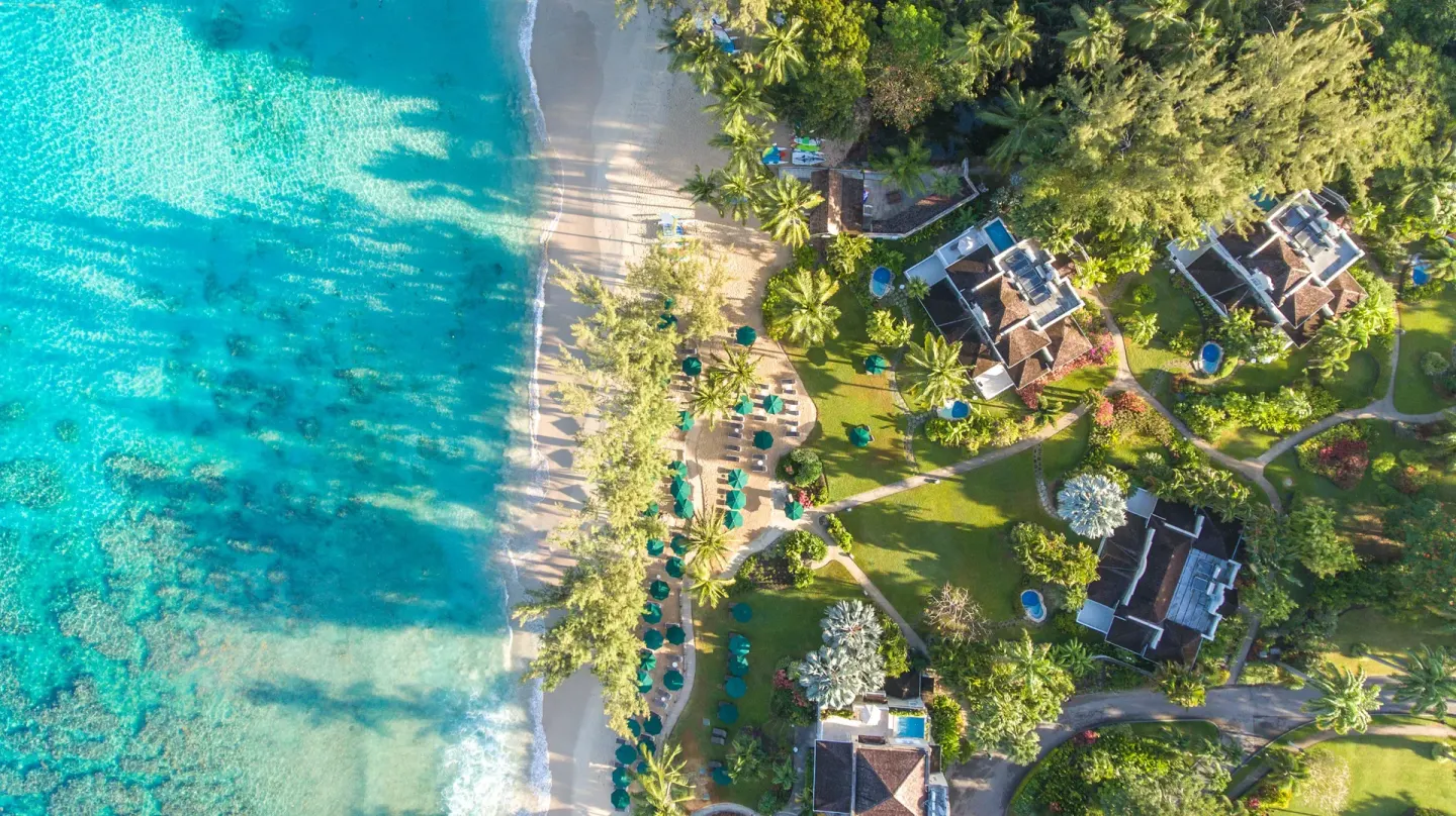 Aerial view of Coral Reef Club gardens, beach loungers, and turquoise shoreline.