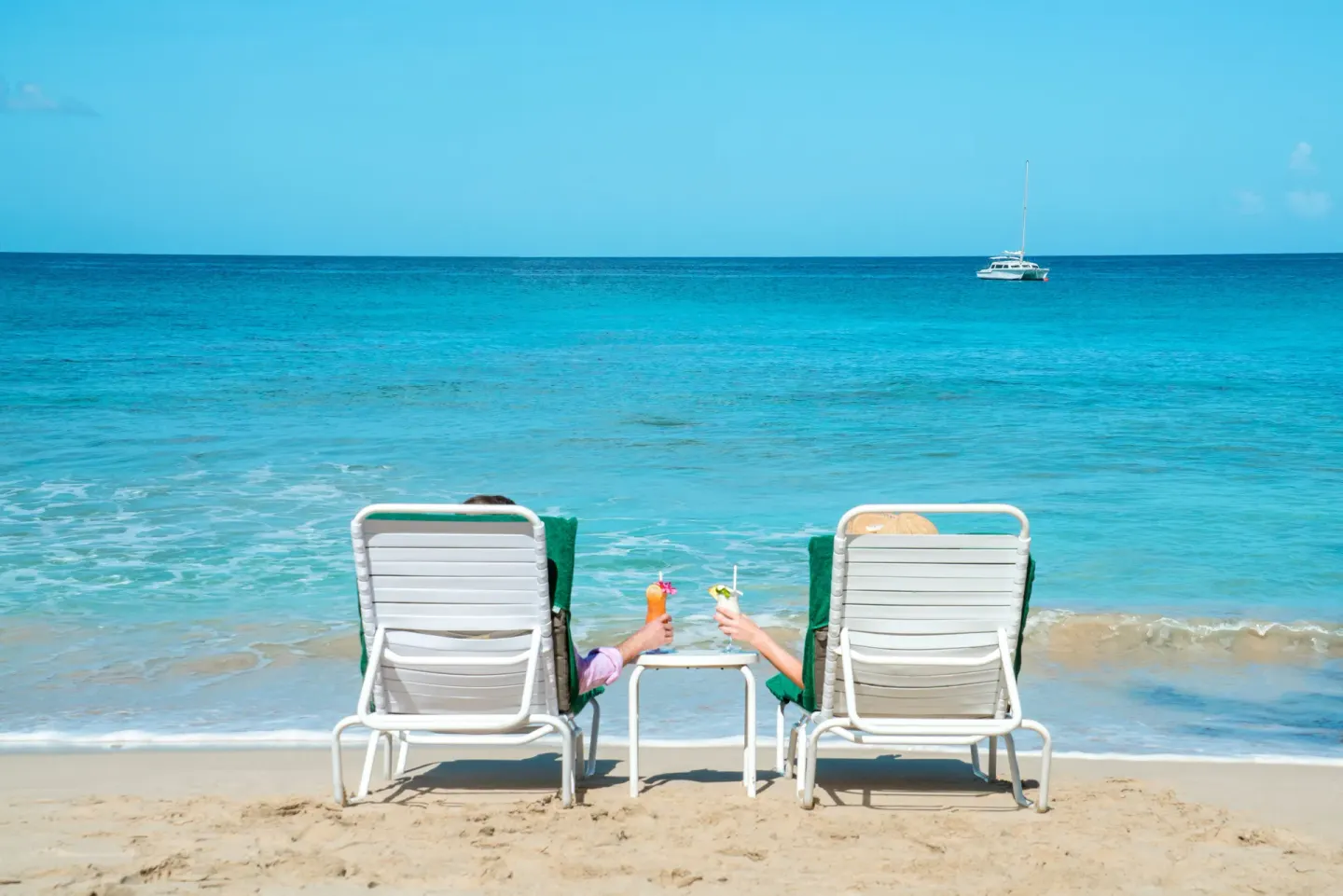 Two beach loungers face the turquoise sea with drinks at Coral Reef Club.