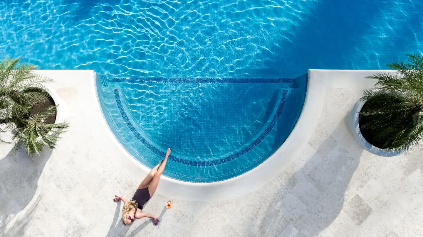 Overhead view of a guest reclining by the curved pool edge at Coral Reef Club.