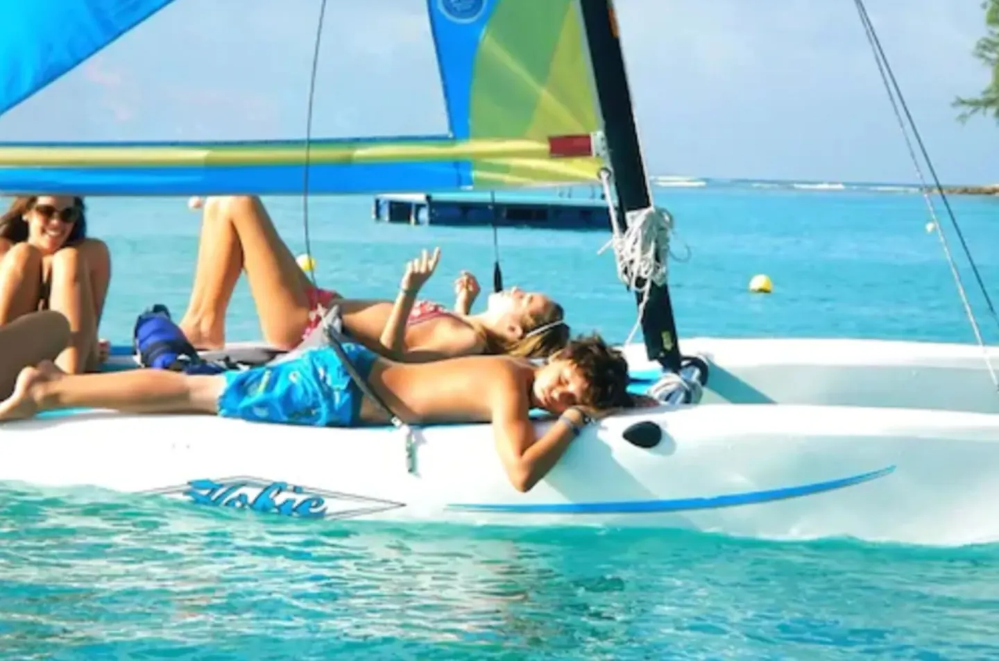 Guests relaxing on a small sailboat in turquoise water at Coral Reef Club.