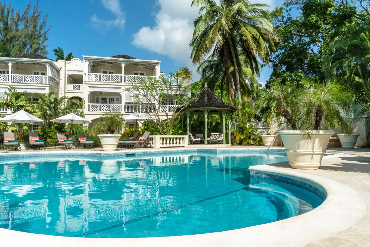 Swimming pool with loungers, umbrellas, palms, and resort balconies at Coral Reef Club.