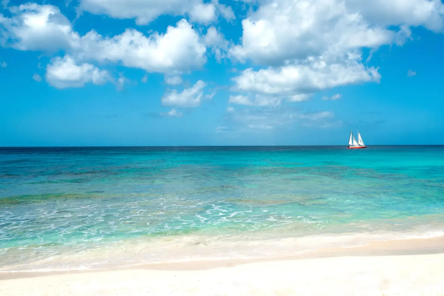 White sand, turquoise sea, and a sailboat offshore at Coral Reef Club.