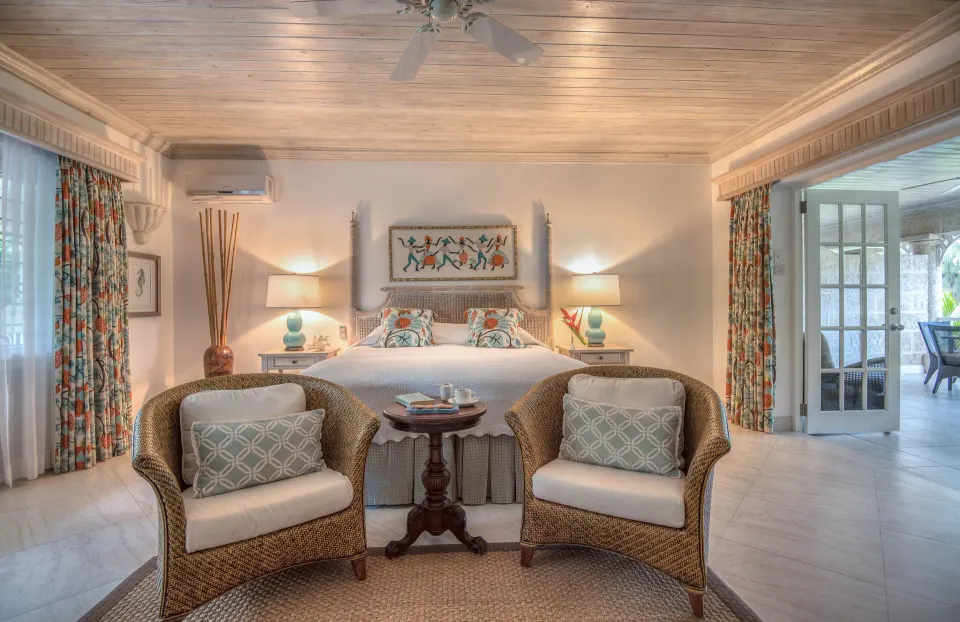 Cottage room with king bed, wicker chairs, and terrace doors at Coral Reef Club.