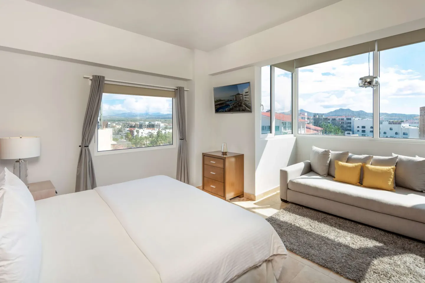 Guest room with bed, sofa, large windows, and city views at Corazón Cabo.