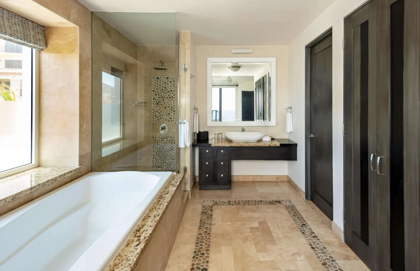 Stone bathroom with soaking tub, glass shower, and vanity at Corazón Cabo.