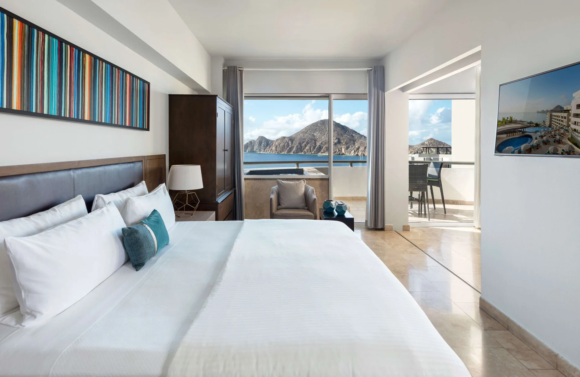 King bed guest room at Corazón Cabo with balcony views of the bay and rocky coastline.