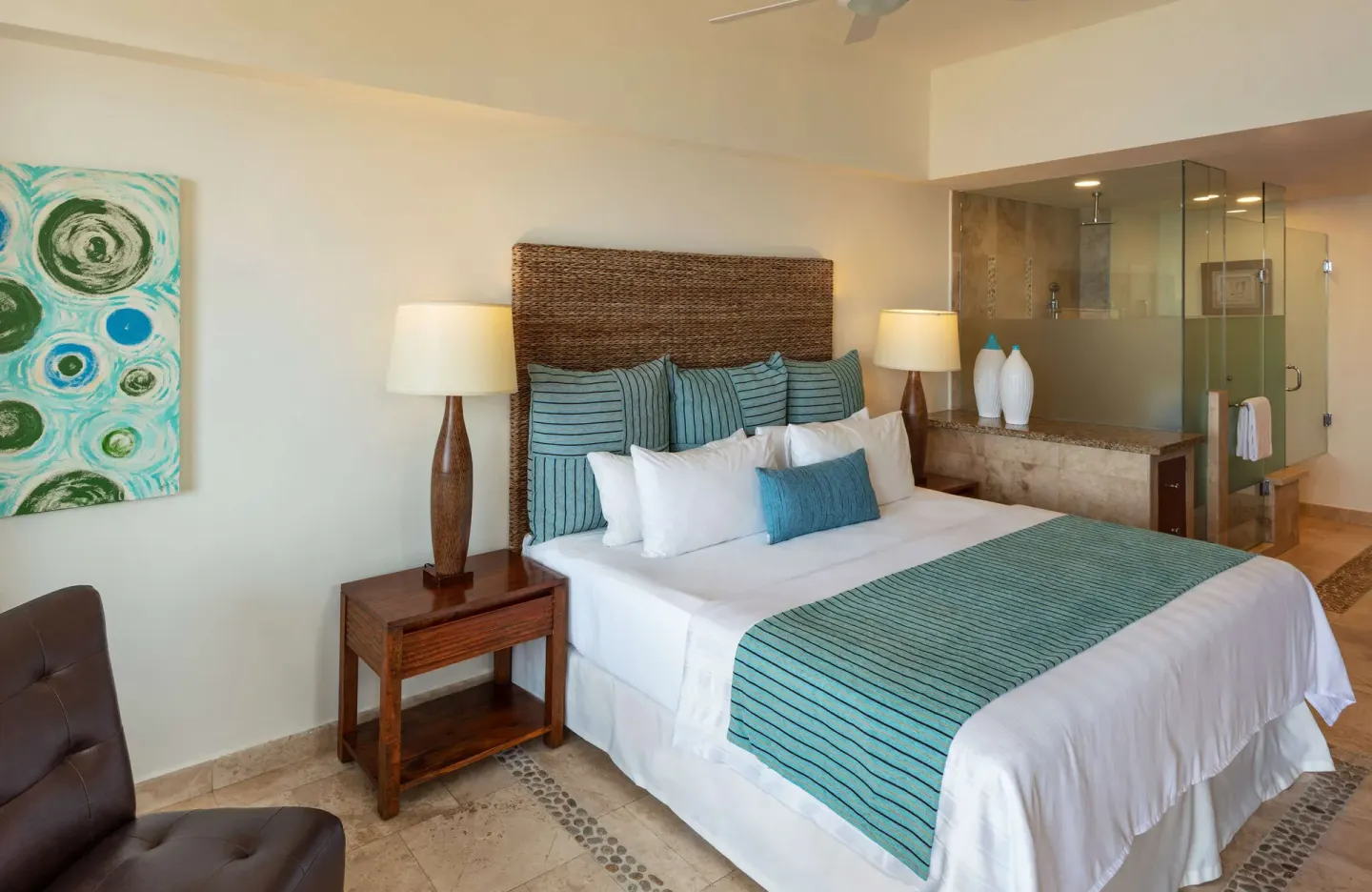 Guest room with king bed, turquoise accents, and glass-walled bathroom at Corazón Cabo.