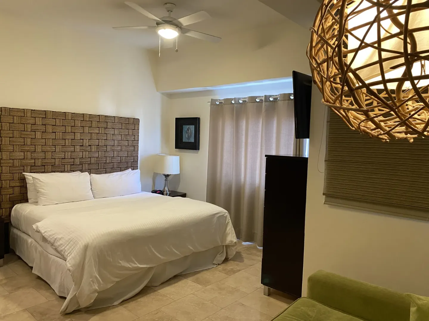 Guest room with king bed, woven headboard, TV, and green sofa at Corazón Cabo.