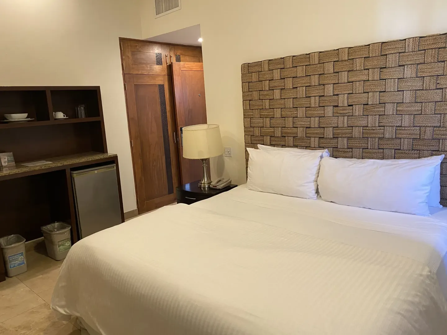 Guest room king bed with woven headboard, minibar cabinet, and entry doors at Corazón Cabo.