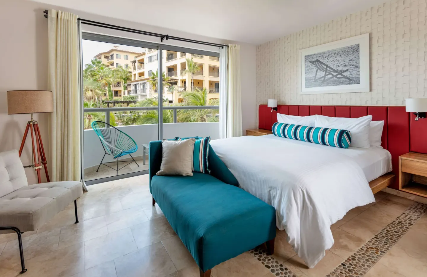 Guest room with king bed, teal chaise, and balcony facing resort grounds at Corazón Cabo.