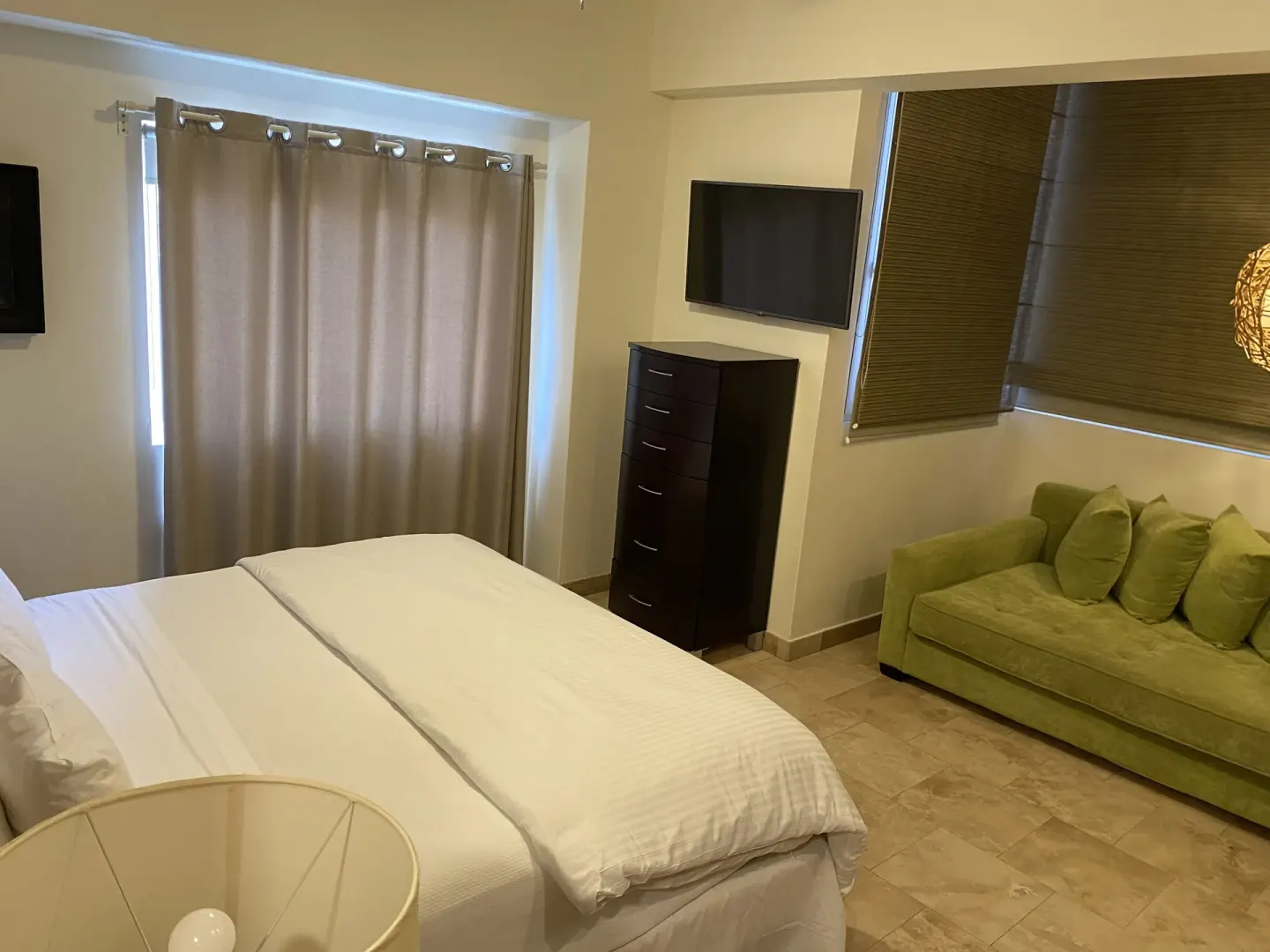 Guest room with king bed, green sofa, dresser, and curtained windows at Corazón Cabo.