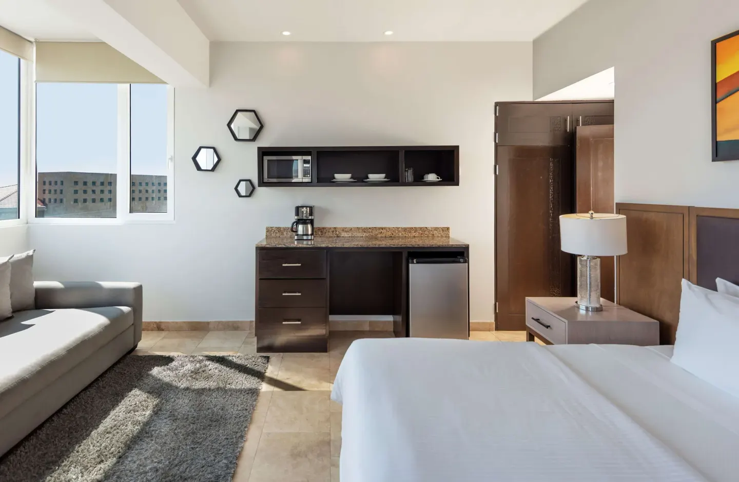 Guest room kitchenette with coffee maker and mini fridge beside the bed at Corazón Cabo.