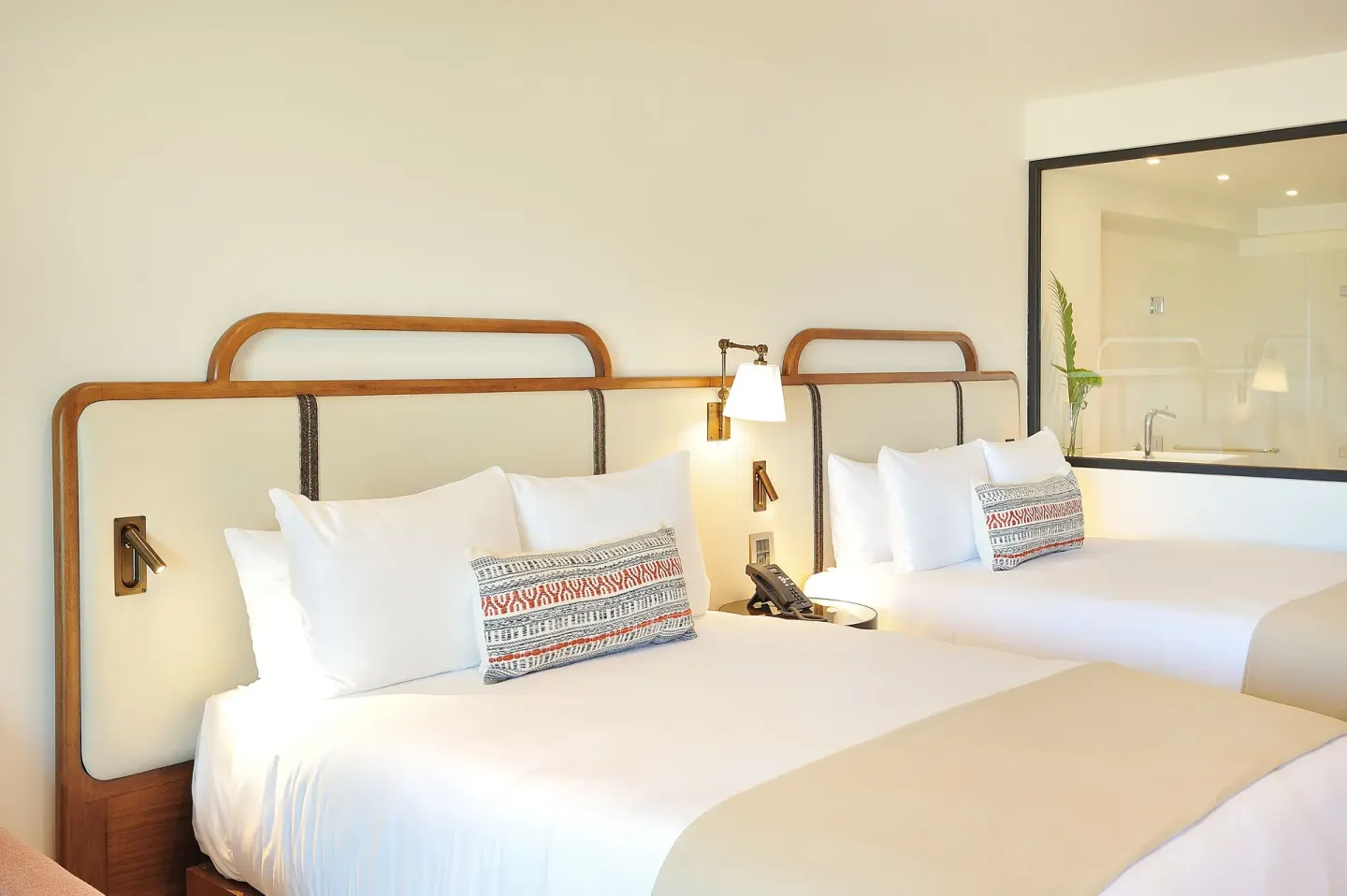 Double bed guest room with two white beds and bathroom window at Corazón Cabo.