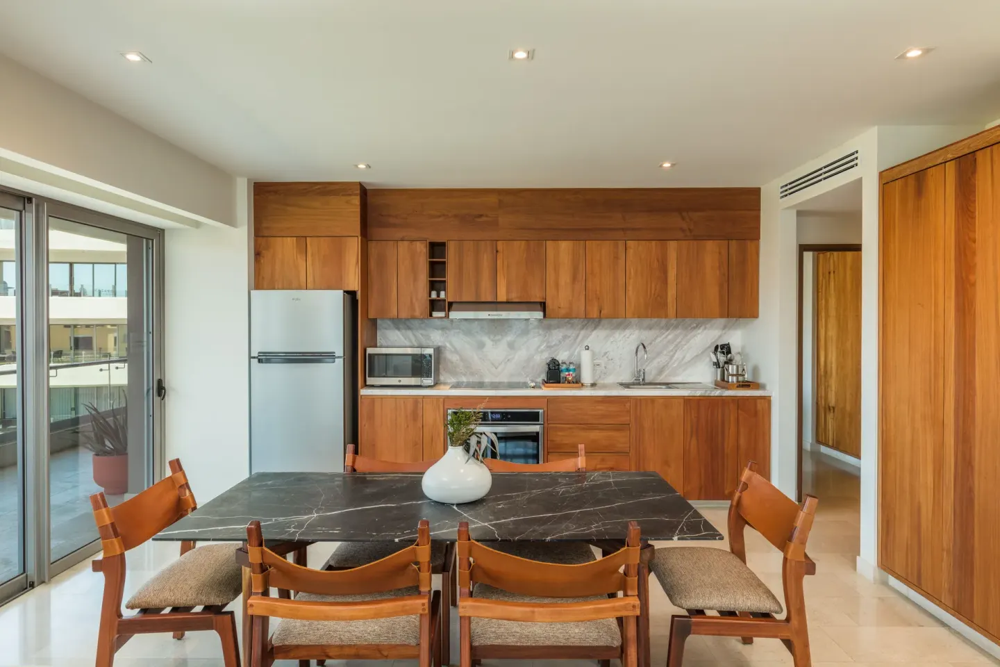 Kitchen and dining area in a suite at Corazón Cabo with wood cabinetry and balcony doors.