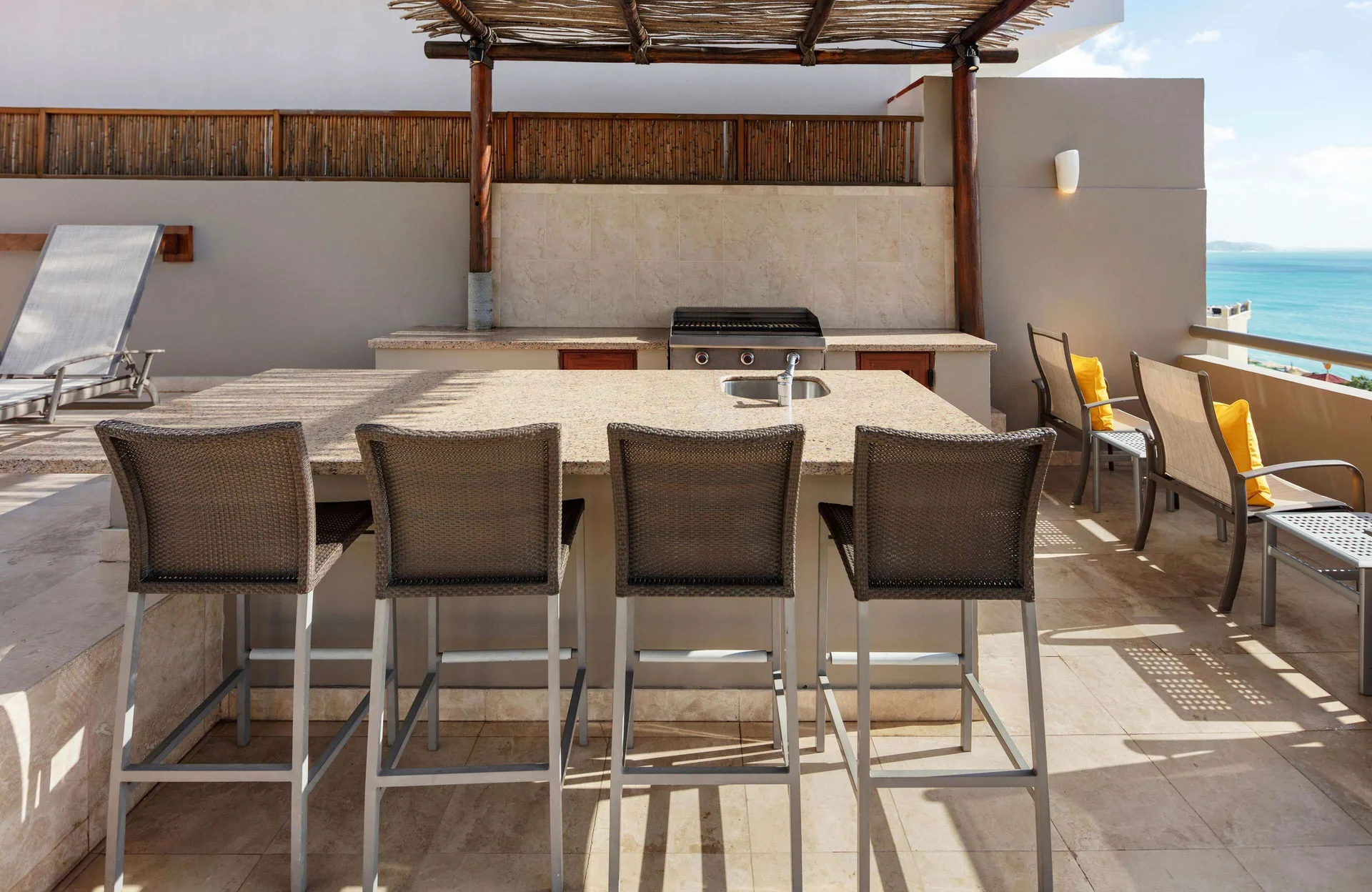 Outdoor terrace bar with grill, stools, and ocean view at Corazón Cabo.