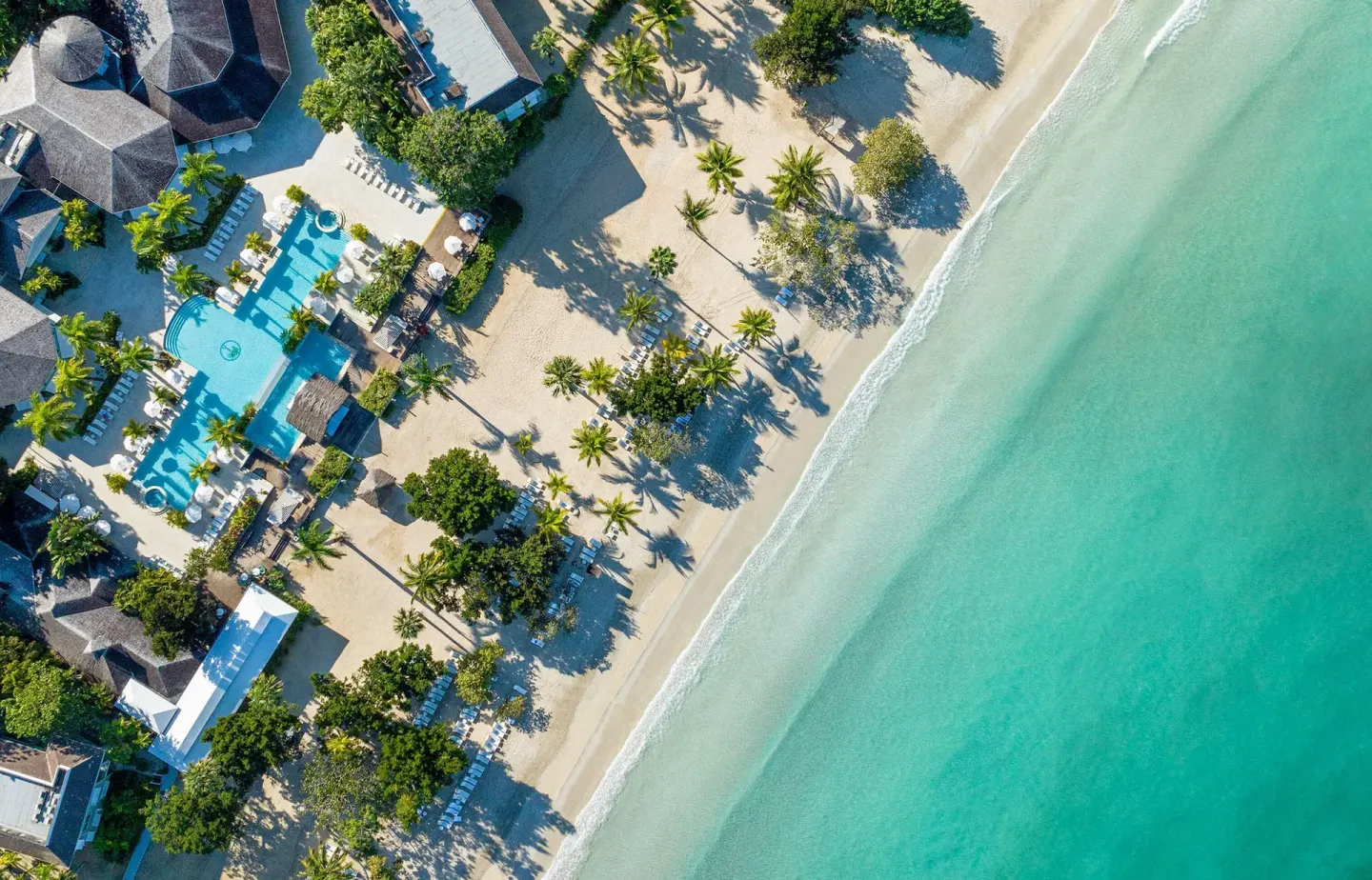 Top-down aerial view of the beach, pool, palms, and turquoise sea at Couples Negril.