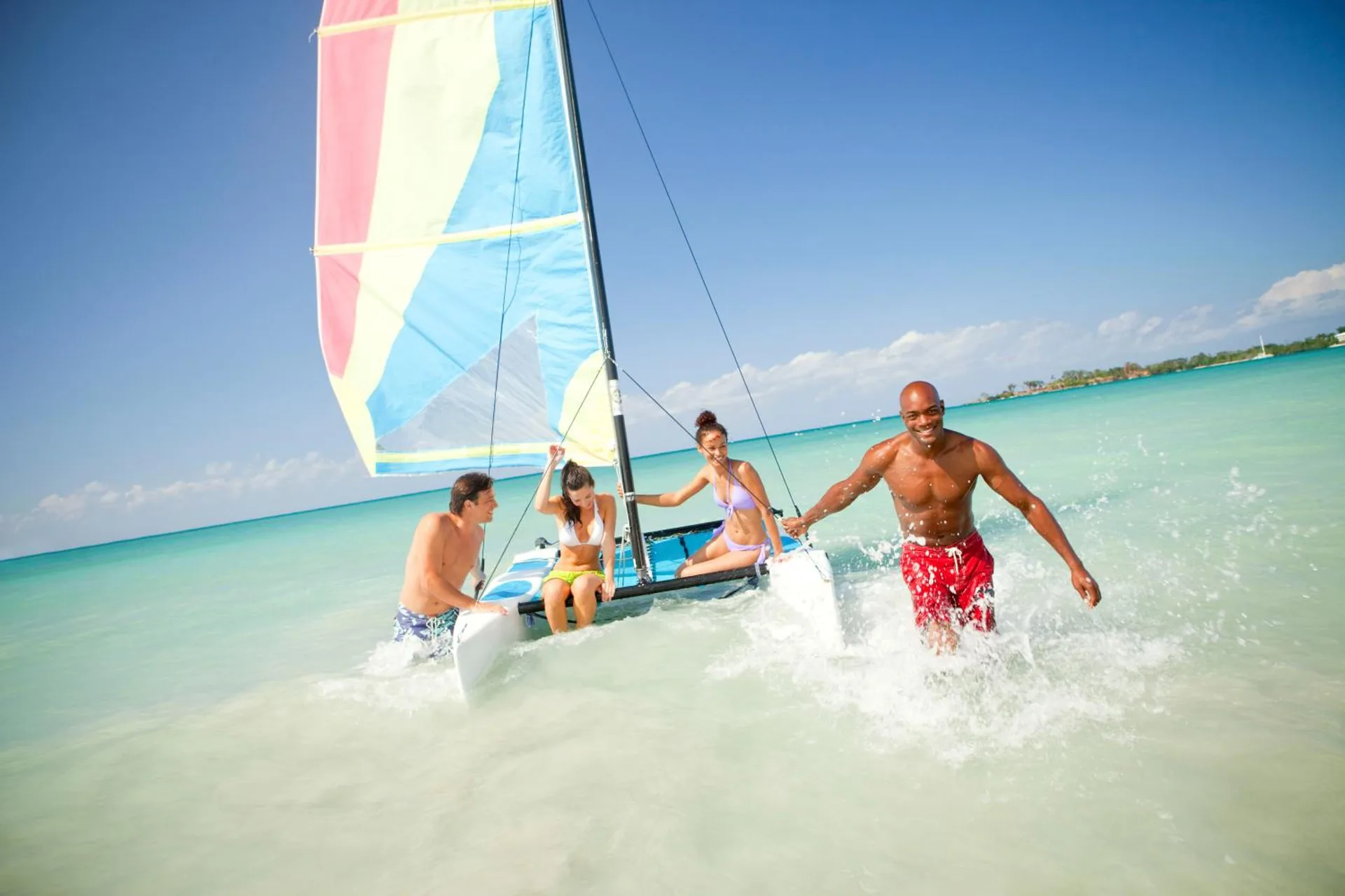 Guests wading beside a small sailboat in clear turquoise water at Couples Negril.