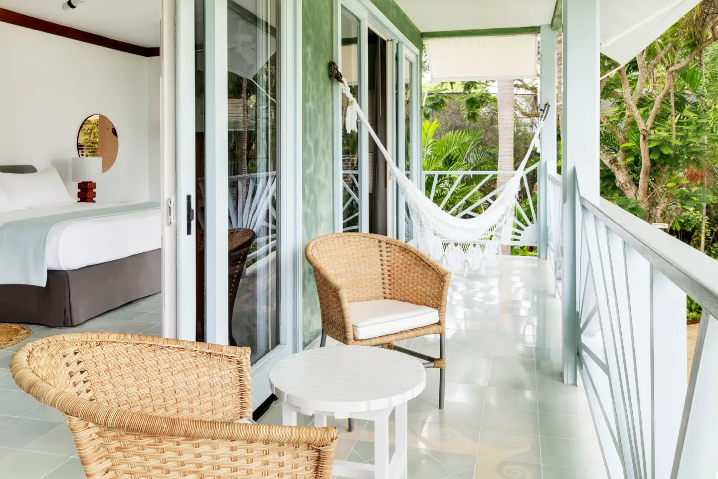Guest room balcony with wicker chairs, a hammock, and a bed inside at Couples Negril.