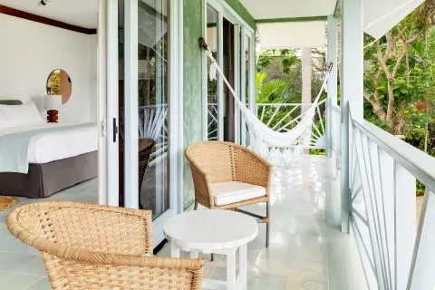 Guest room balcony with wicker chairs, a hammock, and a bed inside at Couples Negril.