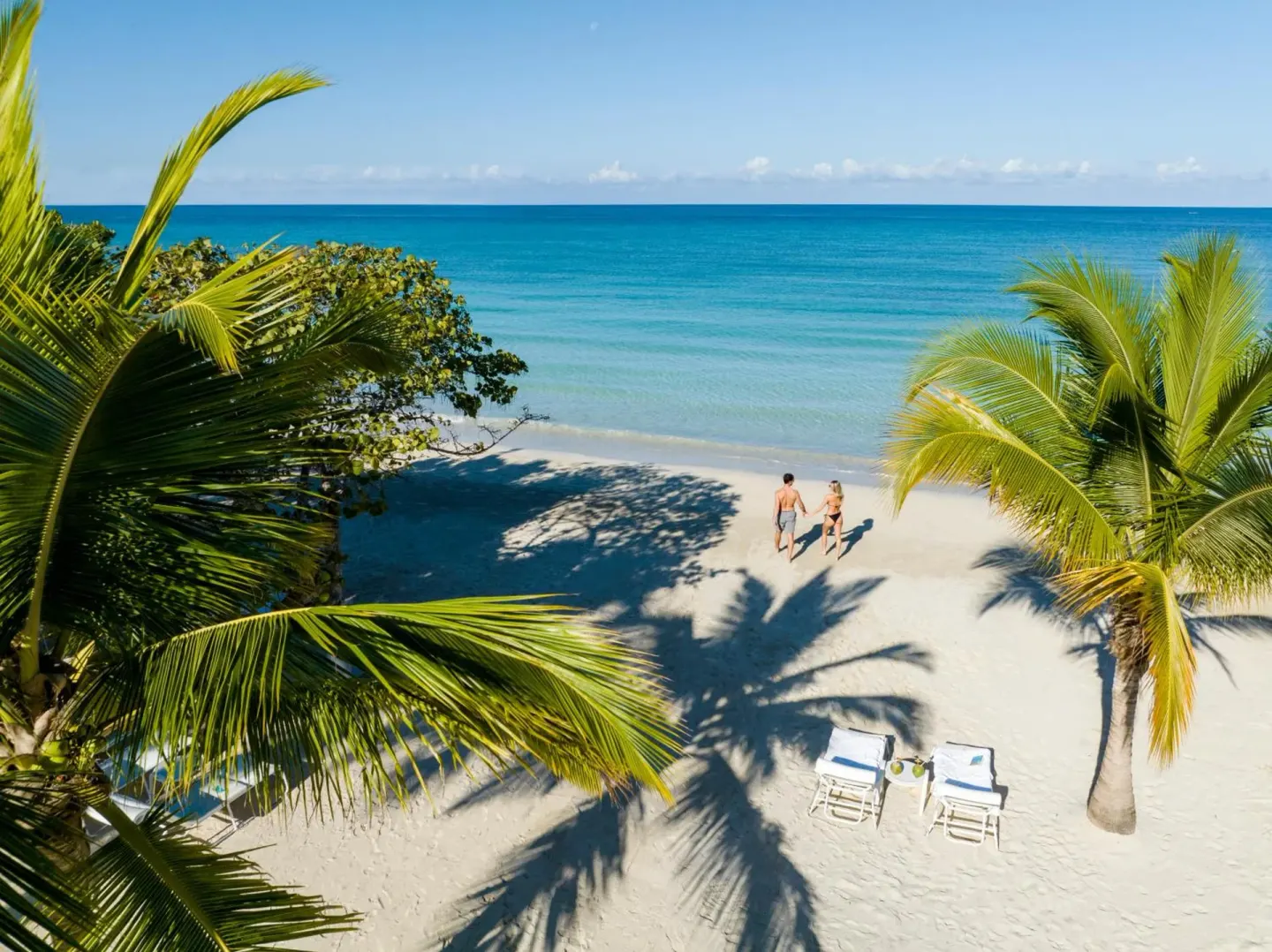 Palm-framed beach with two people walking by the water at Couples Negril.