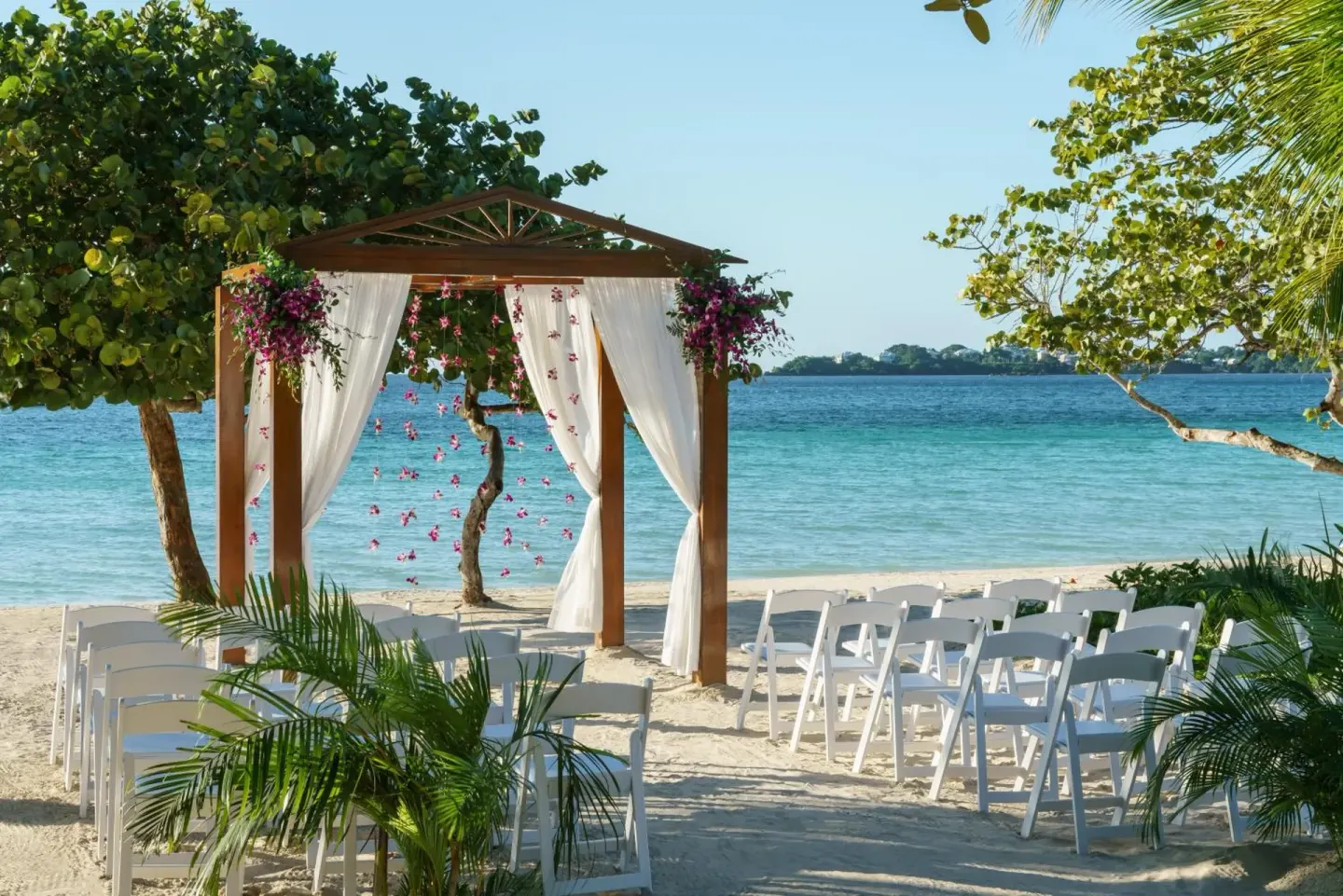 Beach wedding setup with white chairs and floral arch at Couples Negril.