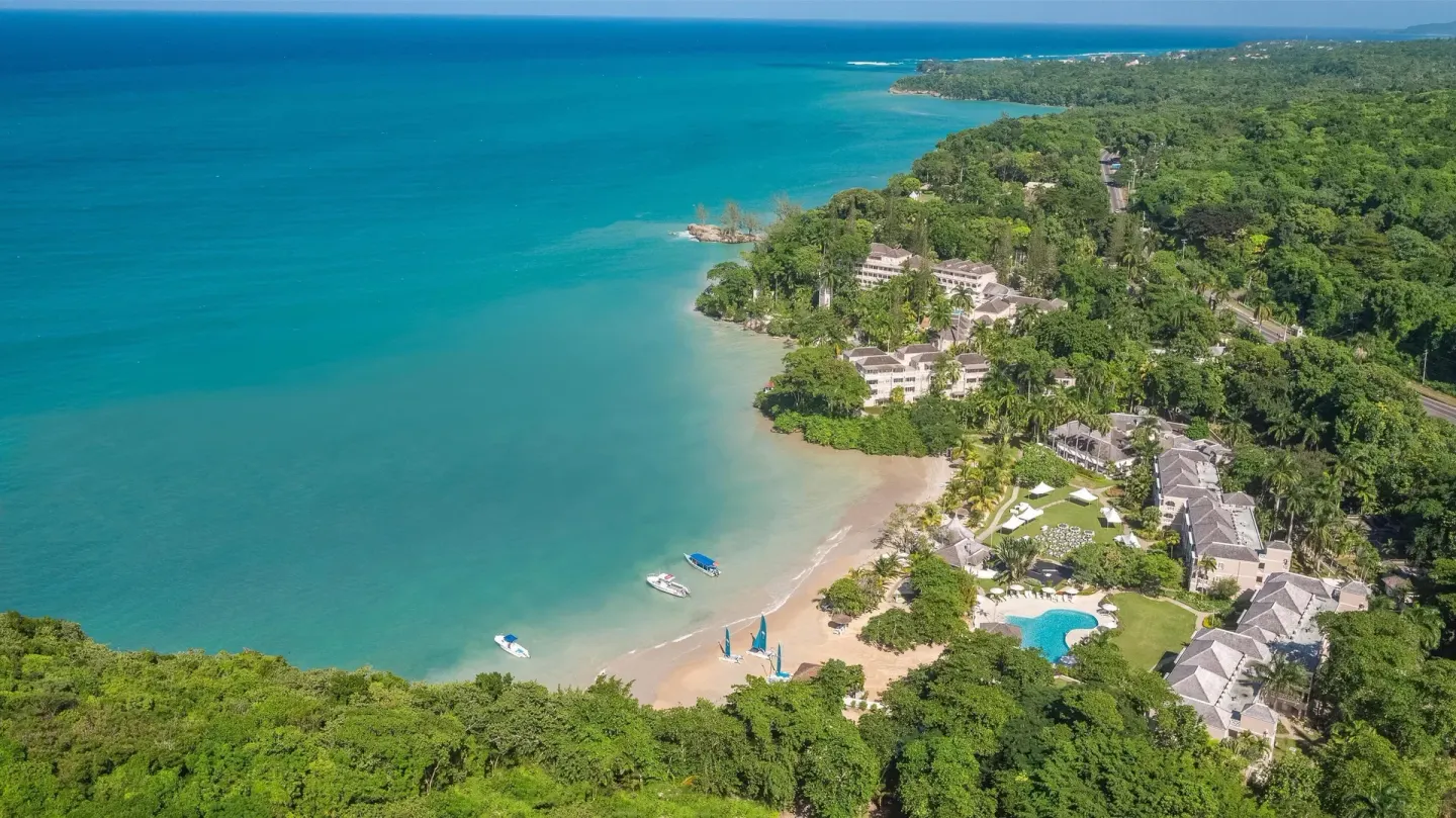 Aerial view of the coastline, beach, pool, and resort buildings at Couples Sans Souci.